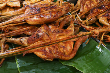 Close-up of several whole, flattened, roasted chickens (likely Thai style 'Gai Yang') held flat by bamboo skewers, resting on vibrant green banana leaves.