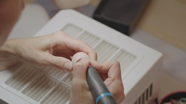 Closeup of artist using rotary tool to drill and smooth silicone doll head near vented surface, showing careful shaping process in detailed doll making