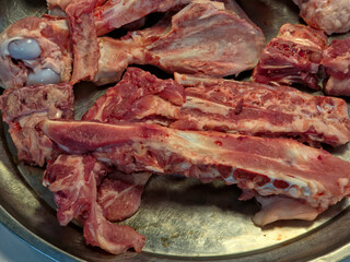 Close-up, overhead view of raw pork bones and meat pieces, including ribs and marrow, arranged in a metal tray for broth or stock preparation.
