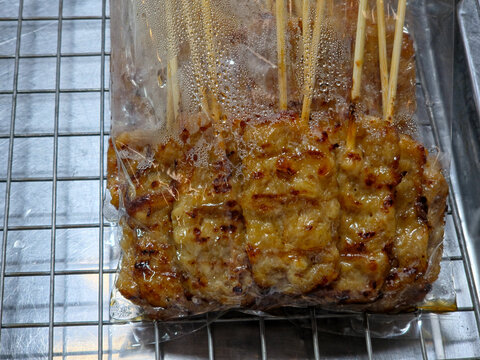 Thai grilled pork skewers (moo ping) packaged in clear plastic bags on a metal cooling rack, ready for sale.