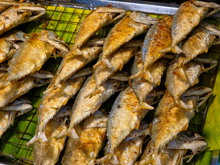 Platter of freshly fried whole mackerel, golden-brown and crispy, arranged on a wire rack over a banana leaf, typical Southeast Asian street food.