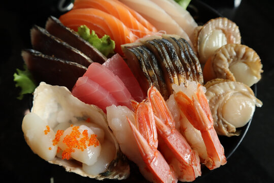 Close-up of a beautifully arranged sashimi platter featuring a variety of fresh seafood such as salmon, tuna, cured mackerel (Shime saba), raw scallops (Hotate), bonito, boiled scallops, and shrimp.
