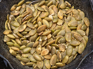 Overhead close-up of a pile of shelled pumpkin seeds (pepitas), contained within a dark bowl.