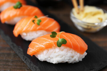 Delicious nigiri sushi with salmon and microgreens on wooden table, closeup