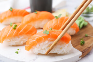 Taking tasty nigiri sushi with chopsticks at white table, closeup