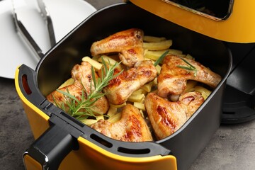 Grilled chicken wings, french fries and rosemary in air fryer on grey table, closeup