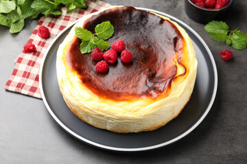 Tasty Basque cheesecake with raspberries and mint on grey textured table, closeup