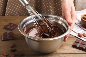 Woman mixing melted chocolate in bowl at wooden table, closeup