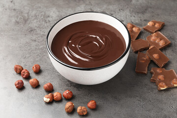 Melted chocolate in bowl, pieces and nuts on grey table, closeup