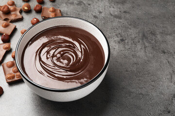 Melted chocolate in bowl and pieces with nuts on grey table, closeup. Space for text