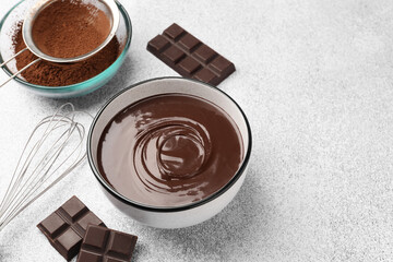 Melted chocolate in bowl, pieces, cocoa powder and whisk on light grey table, closeup. Space for text