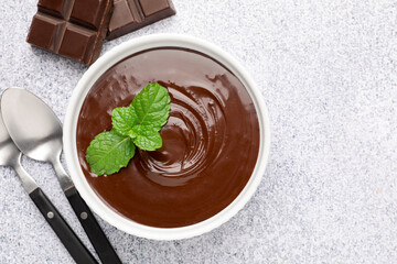 Melted chocolate with mint in bowl, pieces and spoons on light grey table, flat lay
