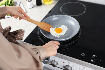 Woman taking fried egg with slotted spatula in kitchen, closeup
