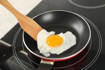 Taking fried egg with wooden spatula in kitchen, closeup