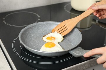 Woman taking fried eggs with slotted spatula in kitchen, closeup
