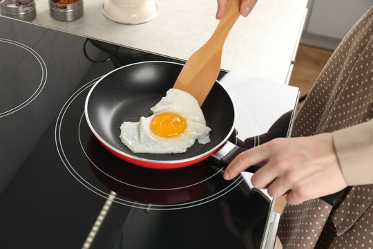Woman taking fried egg with wooden spatula in kitchen, closeup