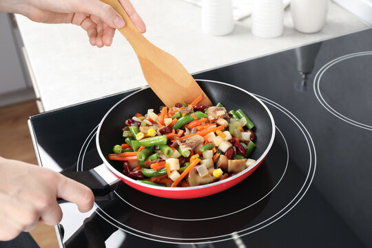 Woman stirring mix of fresh vegetables with wooden spatula in frying pan, closeup - Powered by Adobe