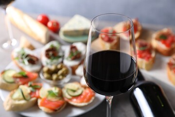 Glass of red wine and tasty bruschettas on grey table, selective focus