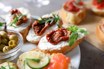 Tasty bruschettas with salmon, cucumber, cream cheese, sun dried tomatoes and olives on grey textured table, closeup