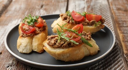 Delicious bruschettas with tuna, tomatoes and arugula on wooden table, closeup