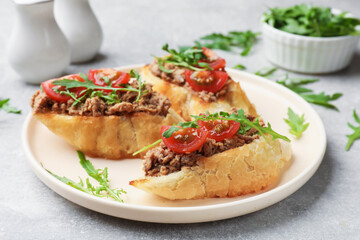 Delicious bruschettas with tuna, tomatoes and arugula on grey table, closeup