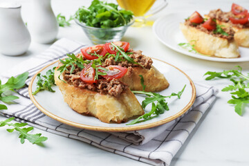 Delicious bruschettas with tuna, tomatoes and arugula on white table, closeup