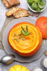 Tasty pumpkin cream soup with seeds and basil served in pumpkin on grey table, flat lay