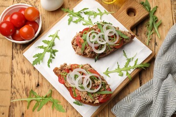 Delicious bruschettas with tuna, tomatoes, onion and arugula on wooden table, flat lay