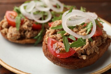 Delicious bruschettas with tuna, tomatoes, onion and arugula on table, closeup