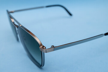 Minimalist retro composition showing sleek sunglasses with polished silver frame, presented in fashion influenced seventies aesthetic over smooth pastel blue backdrop