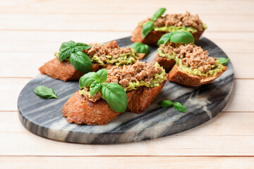 Delicious bruschettas with tuna, avocado and basil on light wooden table, closeup