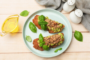 Delicious bruschettas with tuna, avocado and basil served on light wooden table, flat lay