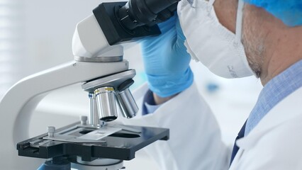 Naklejka premium Microscope and scientist's hands in blue gloves adjusting close up in laboratory set. Medicine, science concept