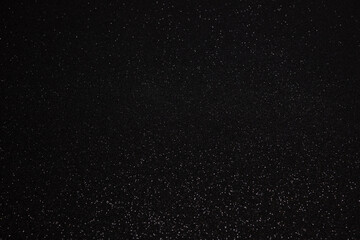 Black glitter background resembling night sky with central focus line, countless sparkling grains create cosmic depth and elegant abstract surface for design
