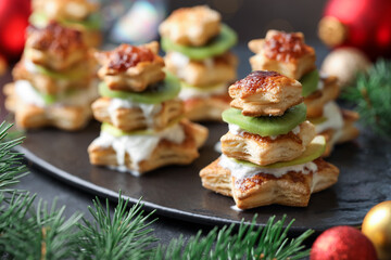 Sweet snacks made of puff pastry, slices of kiwi and Christmas decor on dark table, closeup