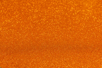 Orange glitter background with golden sparkles in sharp focus at bottom, shimmering grains create radiant festive effect blending softly into blur above