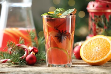 Tasty punch drink in glass, spices, orange, jug and Christmas decor on wooden table against...