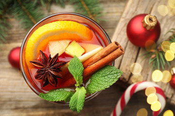 Tasty punch drink in glass, spices and Christmas decor on wooden table, flat lay. Bokeh effect
