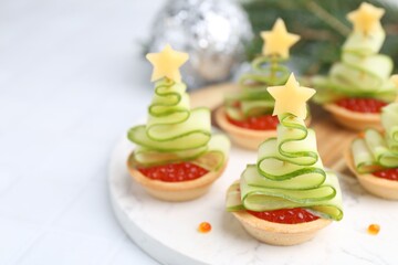 Christmas tree shaped tartlets made with red caviar, cucumber, cheese and festive decor on white table, closeup