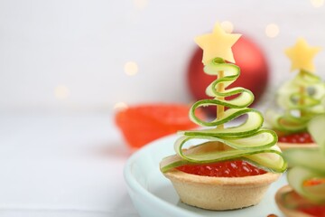 Christmas tree shaped tartlets made with red caviar, cucumber, cheese and festive decor on white table, closeup