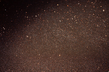 Dark copper glitter surface glowing under scattered light, lower frame textured in focus while upper area dissolves into abstract sparkle and soft blur