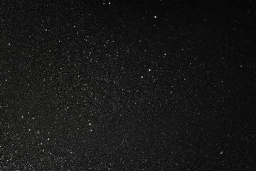 Black textured surface with micro relief focused lower left, diagonal light reveals fine sparkles while glow gradually fades into deep shadow