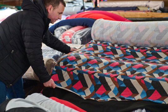 Designer selecting colorful patterned fabric rolls in a textile warehouse, choosing materials for sewing, fabric store, textile industry, material selection, indoor shot.