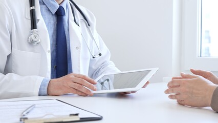 Close-up of doctor man showing information on tablet to patient woman during medical visit,...