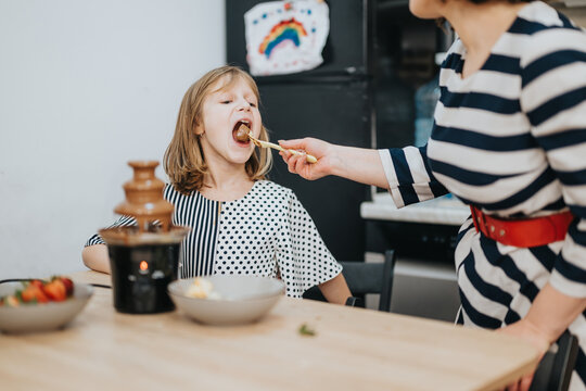 A joyful moment as a mother shares a dessert treat with her smiling daughter at home. A warm and family-oriented scene depicting a nurturing and cheerful environment. - Powered by Adobe