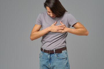 Woman holding chest with both hands, bending forward in pain, neutral background