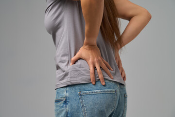 Side close-up view of woman pressing lower back in pain, concept of backache