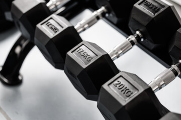 High-resolution close-up of 17.5kg and 20kg hex dumbbells with metal grips on a gym rack. Fitness equipment with clean design and ample copy space