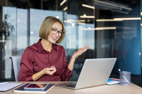 Confident businesswoman smiling and gesticulating during an online video conference, discussing business with colleagues while working remotely from a modern office workspace