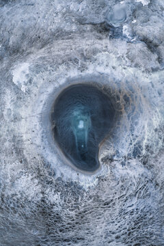 Aerial view of a mesmerizing, frosty landscape reveals a striking, turquoise pool nestled within icy terrain, a jewel of geothermal wonder, Geothermal Areas, Iceland.